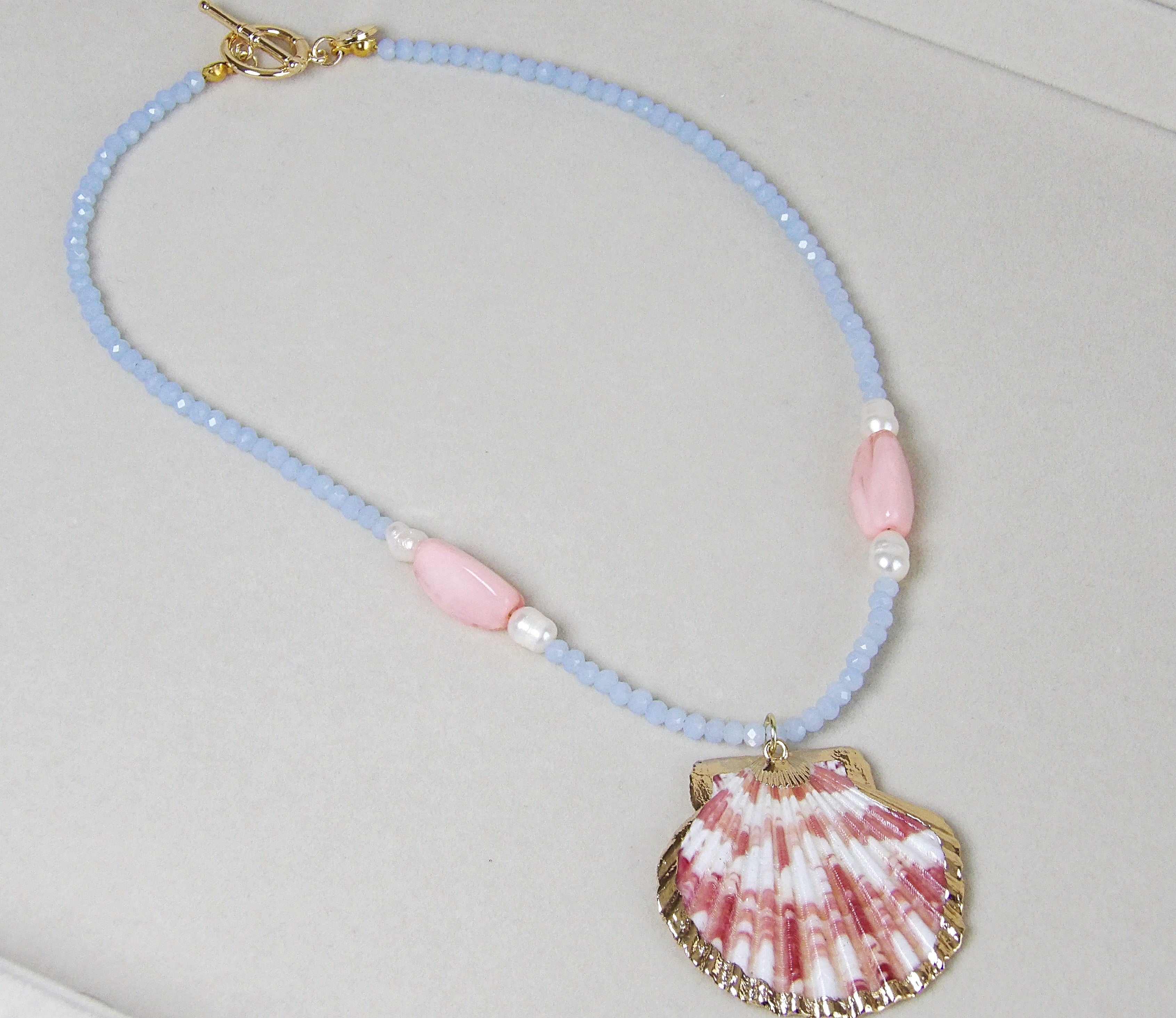 Handmade beaded shell necklace with baby blue beads, pink gemstone accents, freshwater pearls, and gold-trimmed shell pendant, beach jewelry.